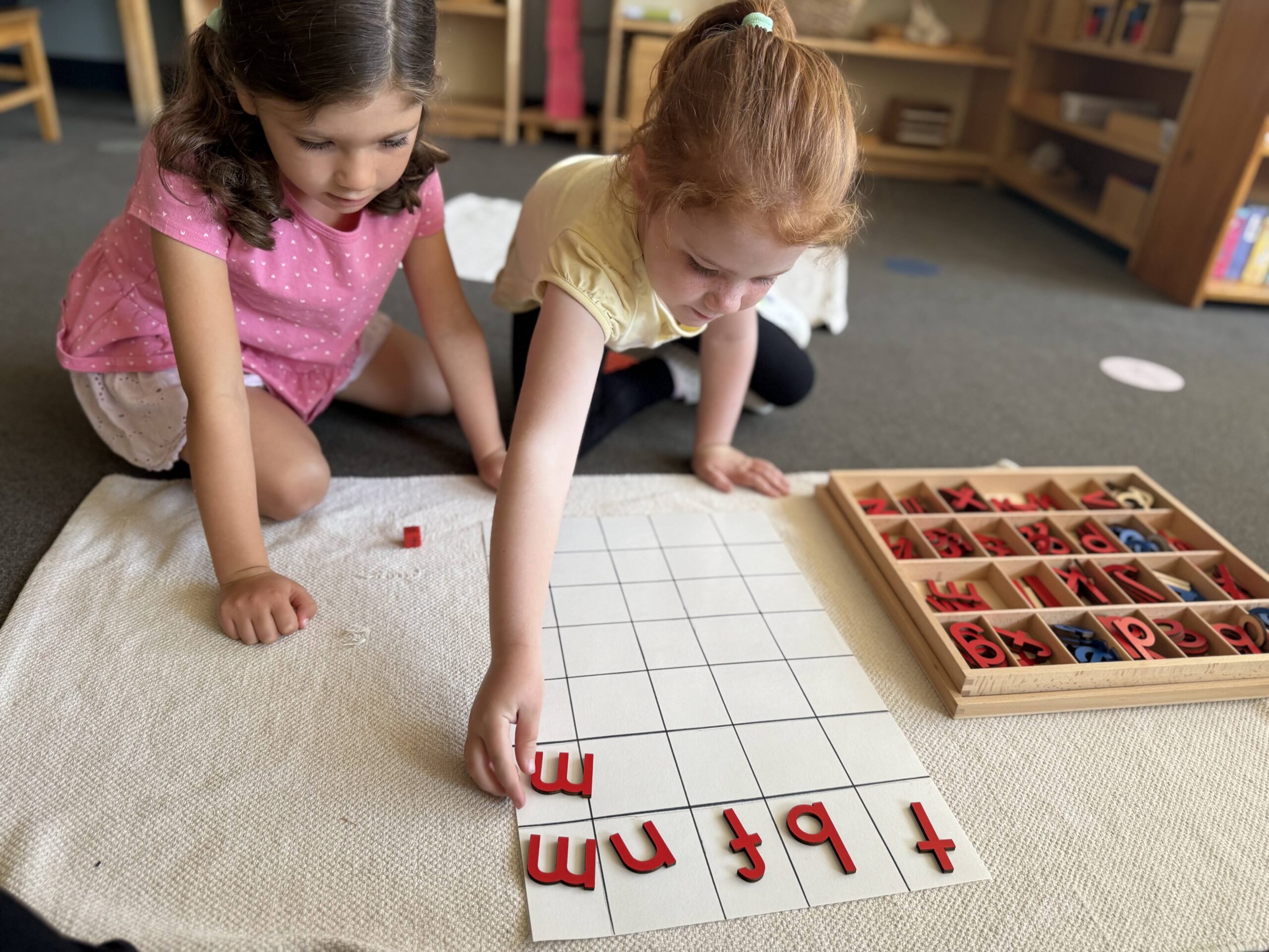 2 students arrange letters in a blank grid on the floor